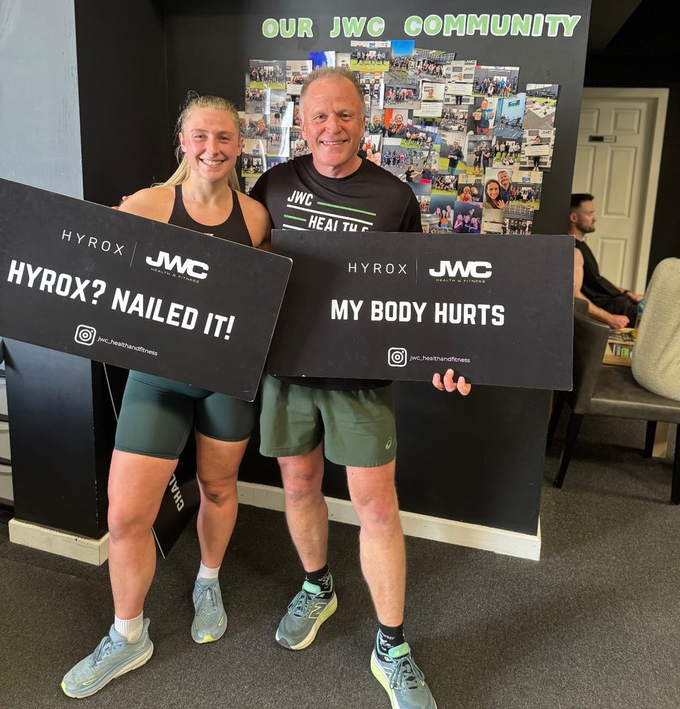Two smiling participants holding 'HYROX? Nailed it!' and 'My body hurts' signs after a JWC simulation