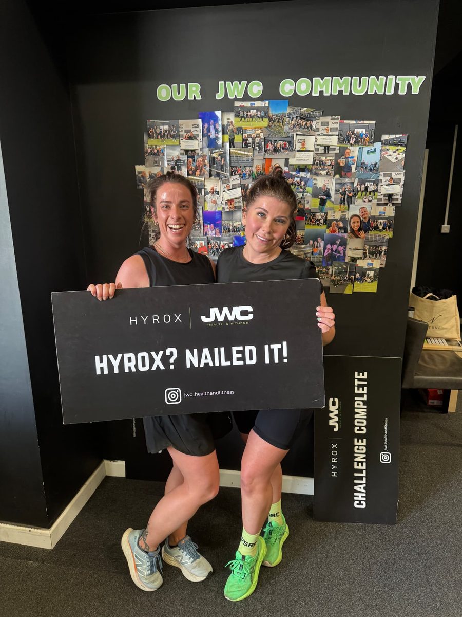 Two participants laughing together and holding a 'HYROX? Nailed it!' sign after their simulation at JWC